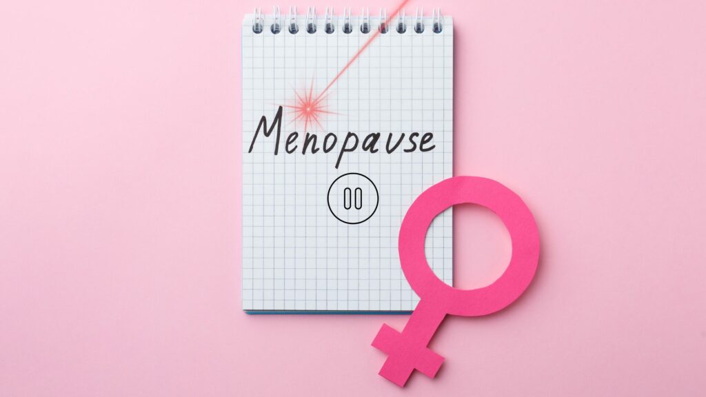 Carnet avec le mot ménopause écrit, entouré du signe pause et du symbole féminin, traversé par un rayon laser illustrant la laserothérapie comme solution naturelle pour retrouver équilibre et bien-être