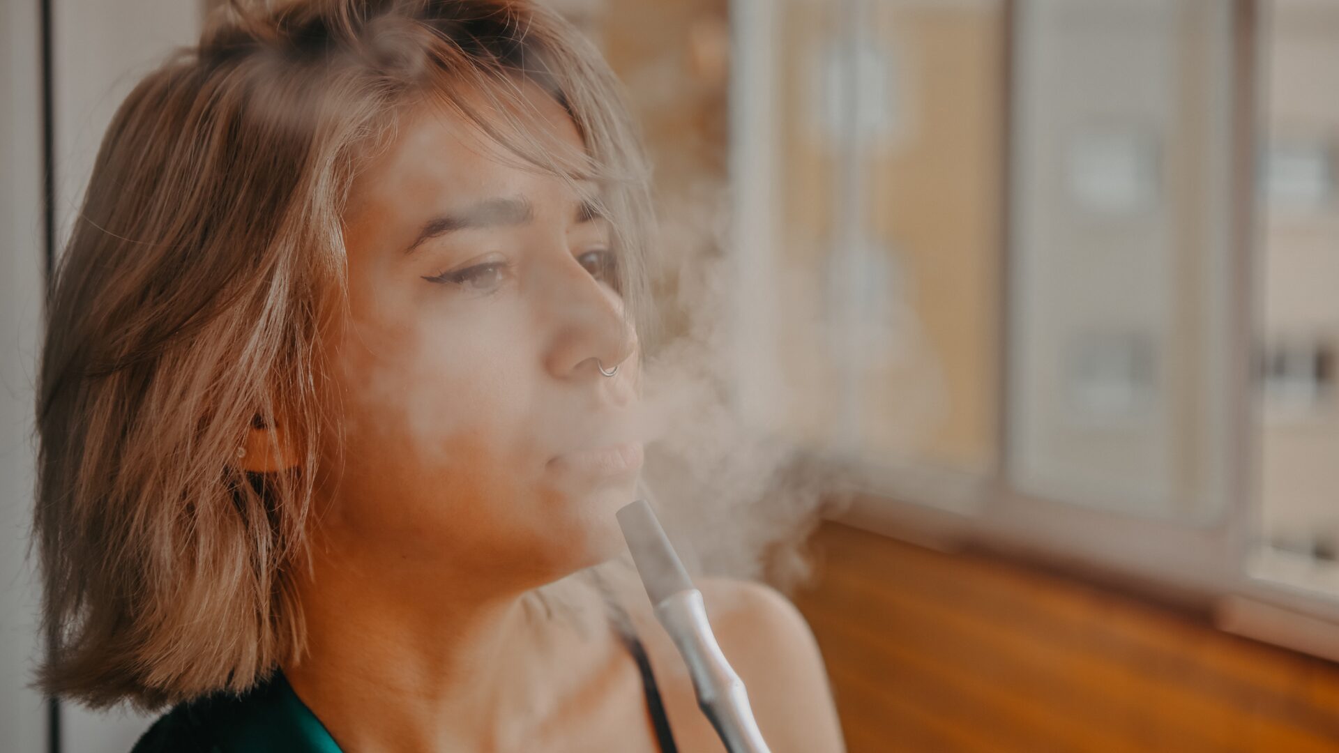 Femme fumant une chicha et expirant un nuage de fumée, symbole de l’addiction au tabac et de la peur d’arrêter de fumer par crainte de la prise de poids, une inquiétude accompagnée par les solutions naturelles LaserAddict.